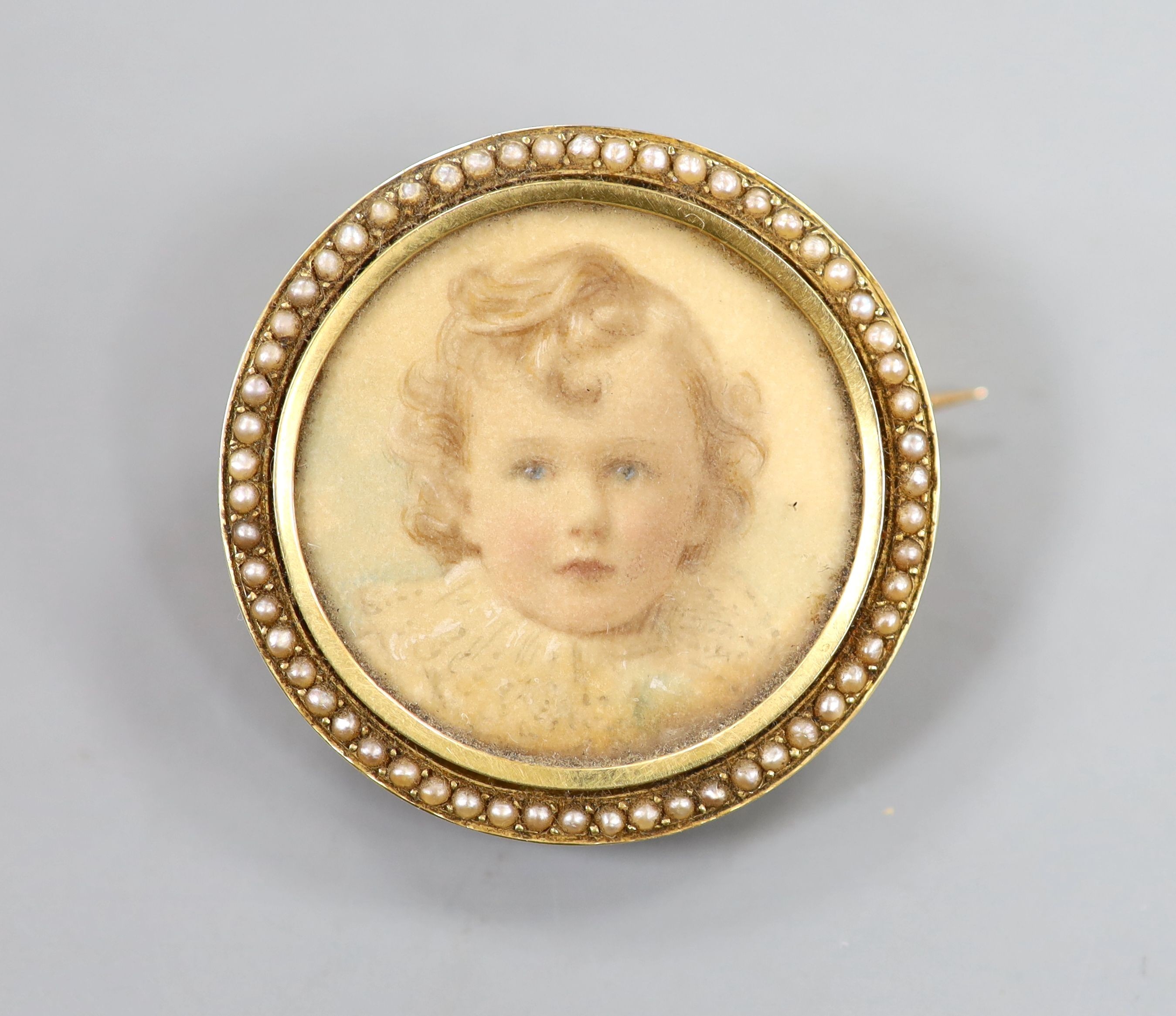 An early 20th century yellow metal and split pearl set circular brooch, inset with portrait of a young, verso with hair beneath a glazed panel, 34mm, gross weight 11.4 grams.